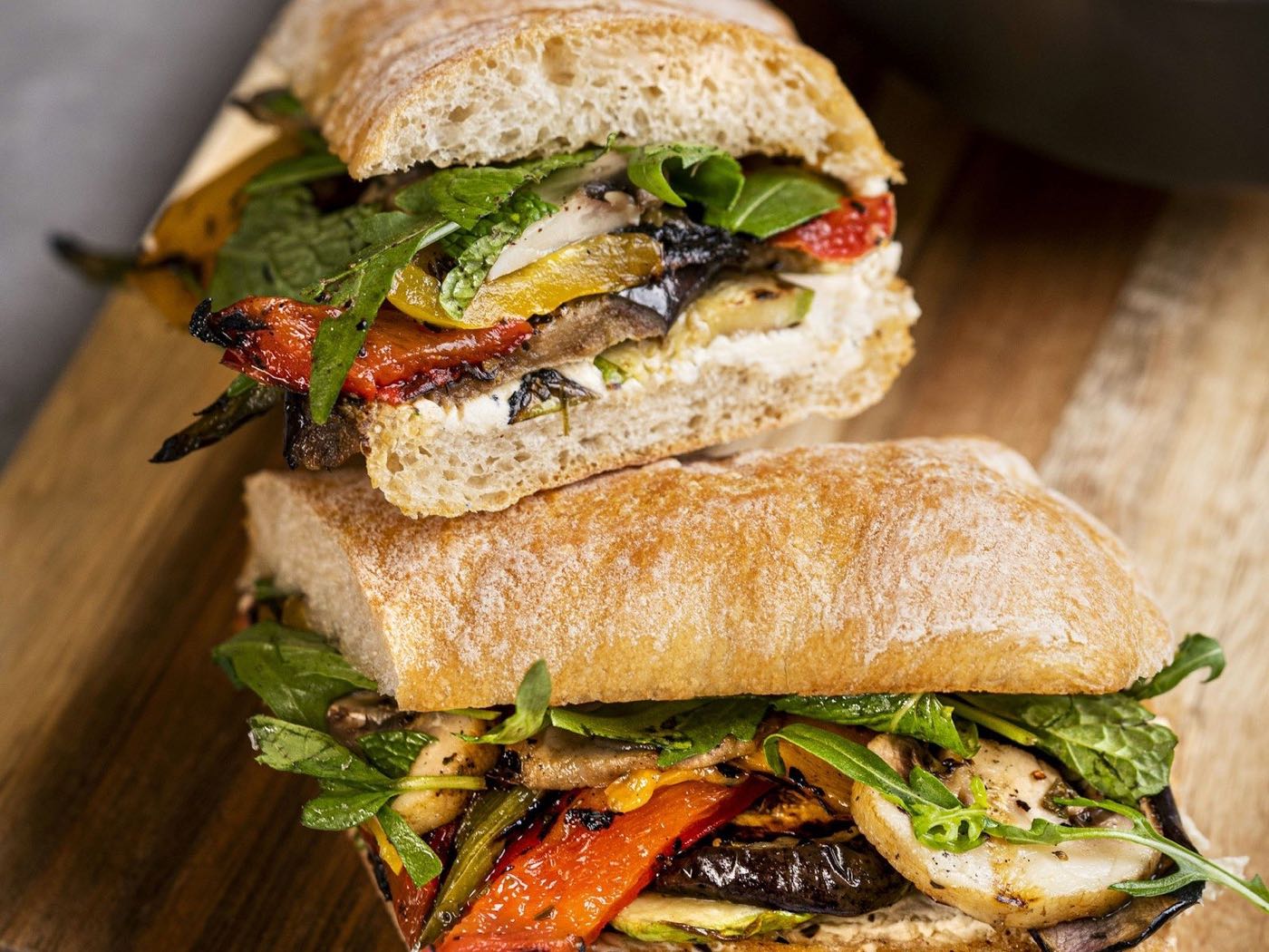 Grilled vegetable sandwich on crusty bread, cut in half on a wooden board