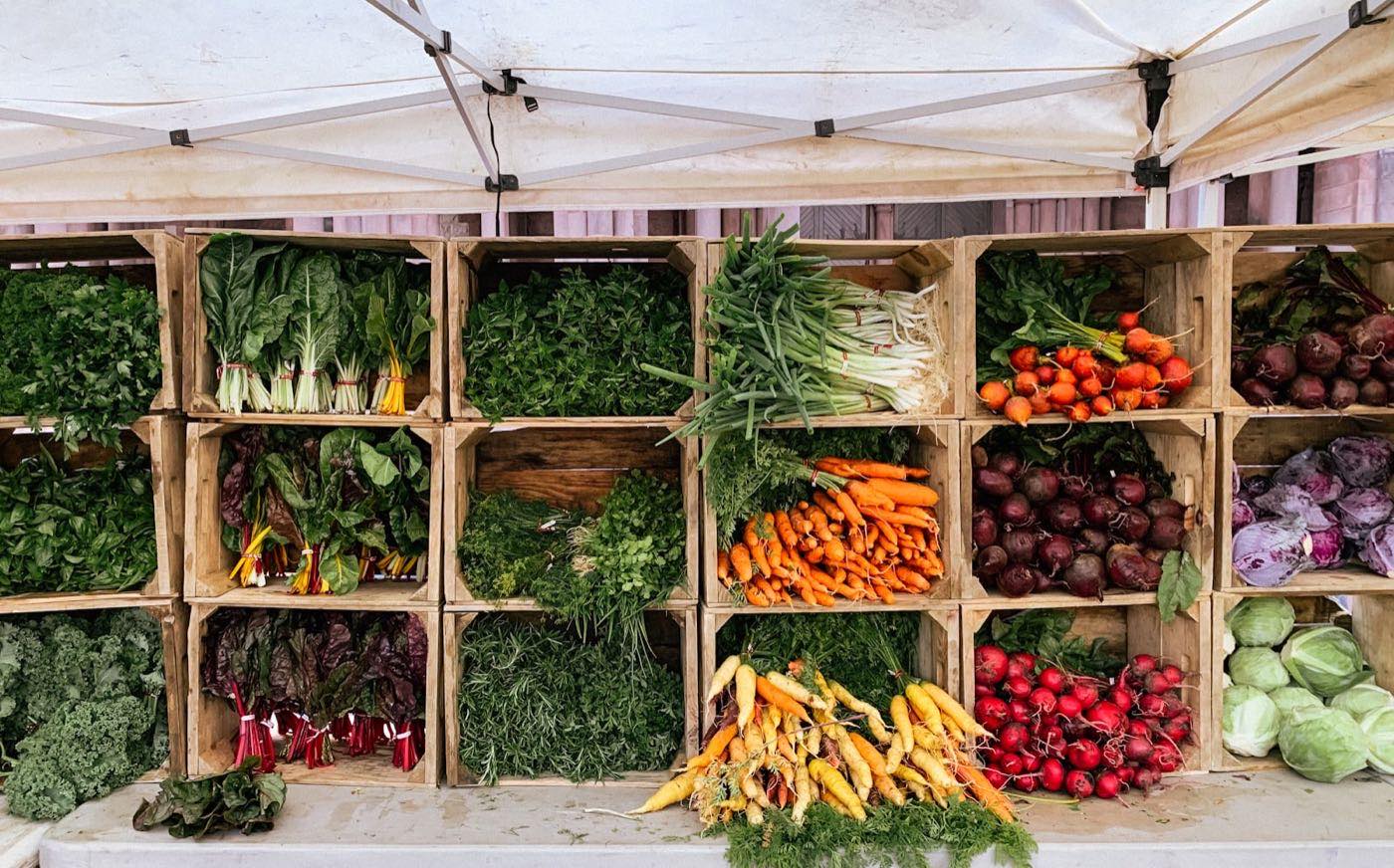 Wooden crates stacked with fresh vegetables and greens at a small market